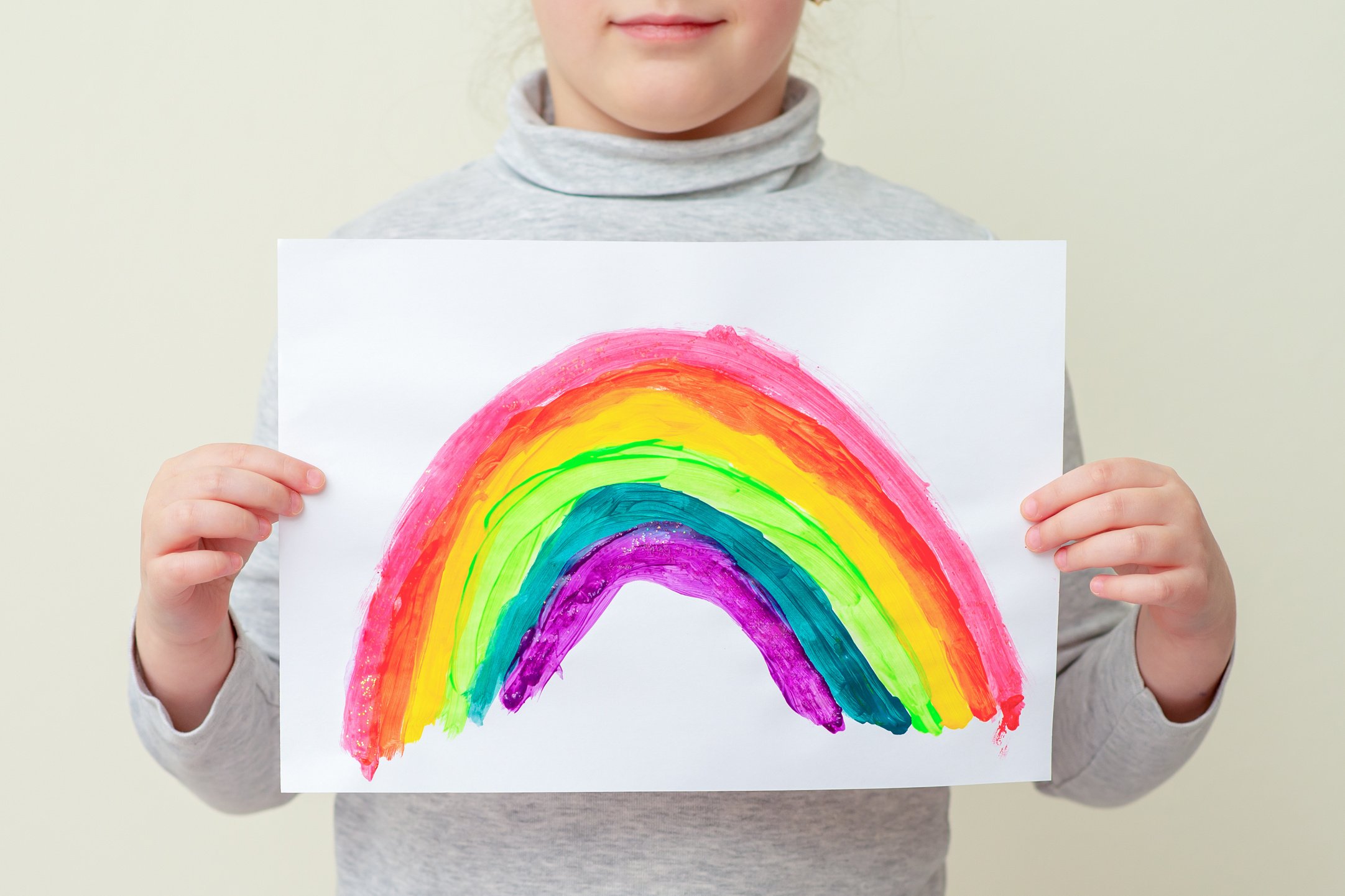 Kid holds drawn rainbow.